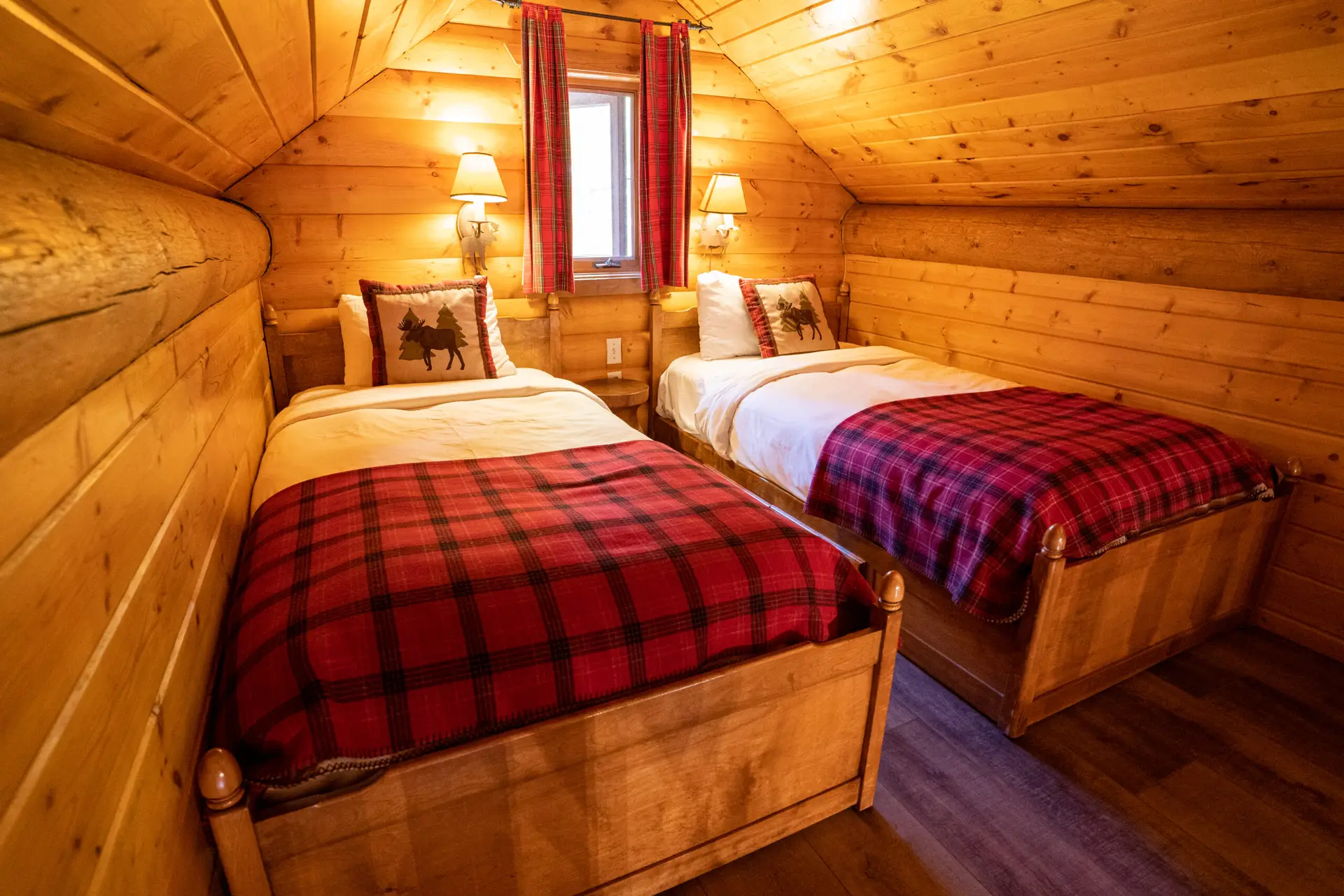 Cozy loft bedroom with two twin beds, plaid blankets, and log walls at Basecamp Baker Creek.