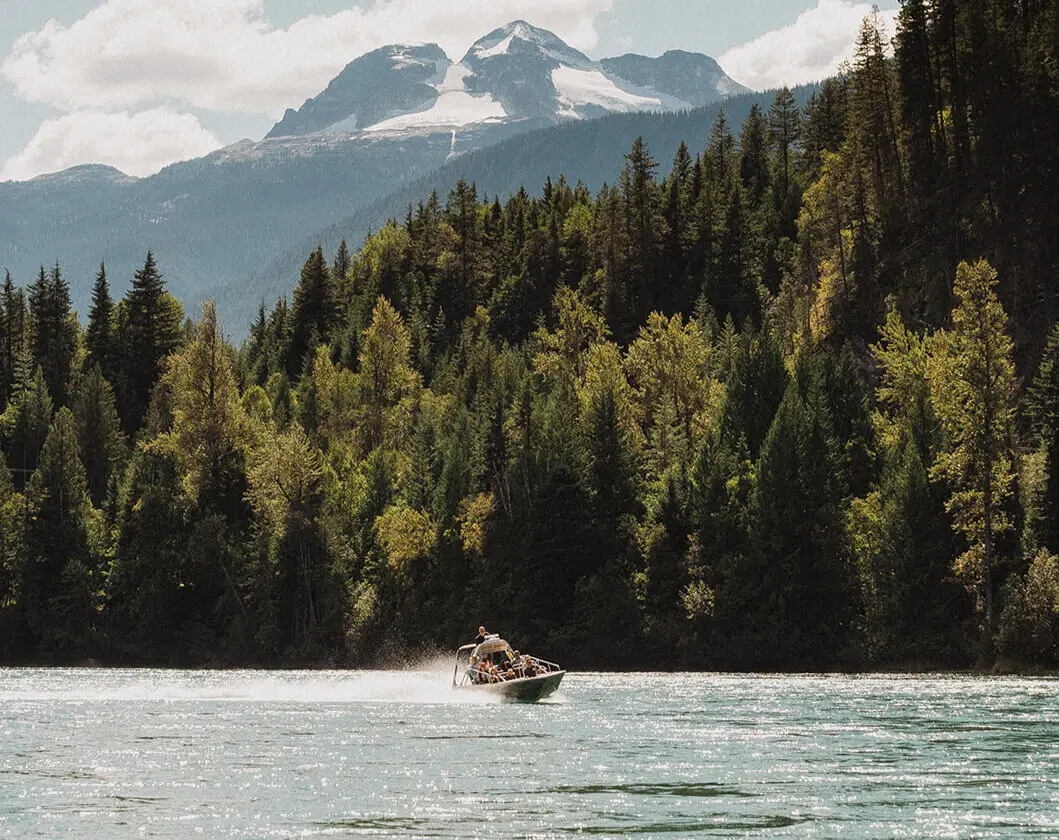 Revy Jets boat speeding across a lake with mountains and forest in the background.