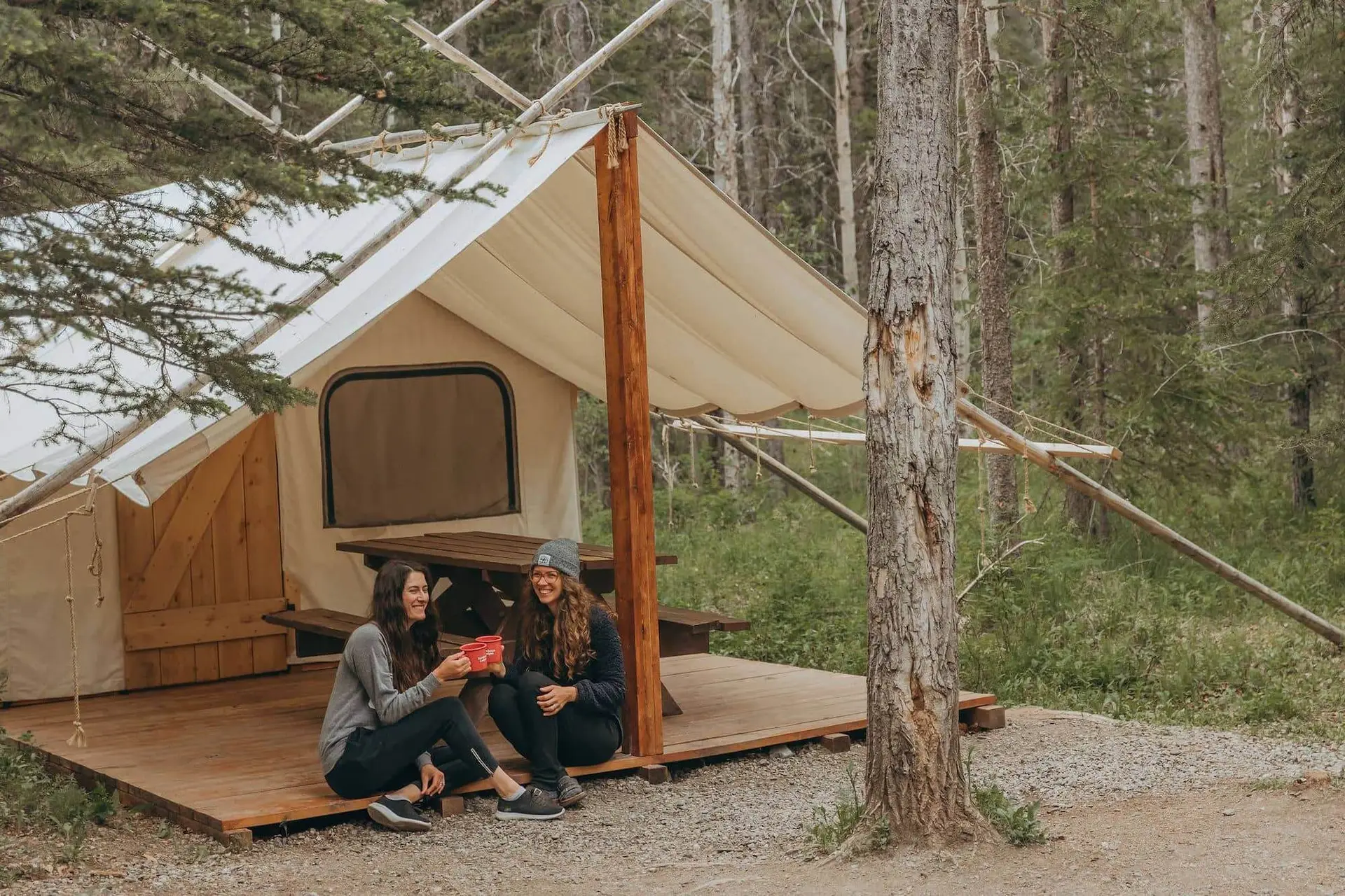 Two women enjoy coffee on the deck of a glamping tent at Sundance by Basecamp.