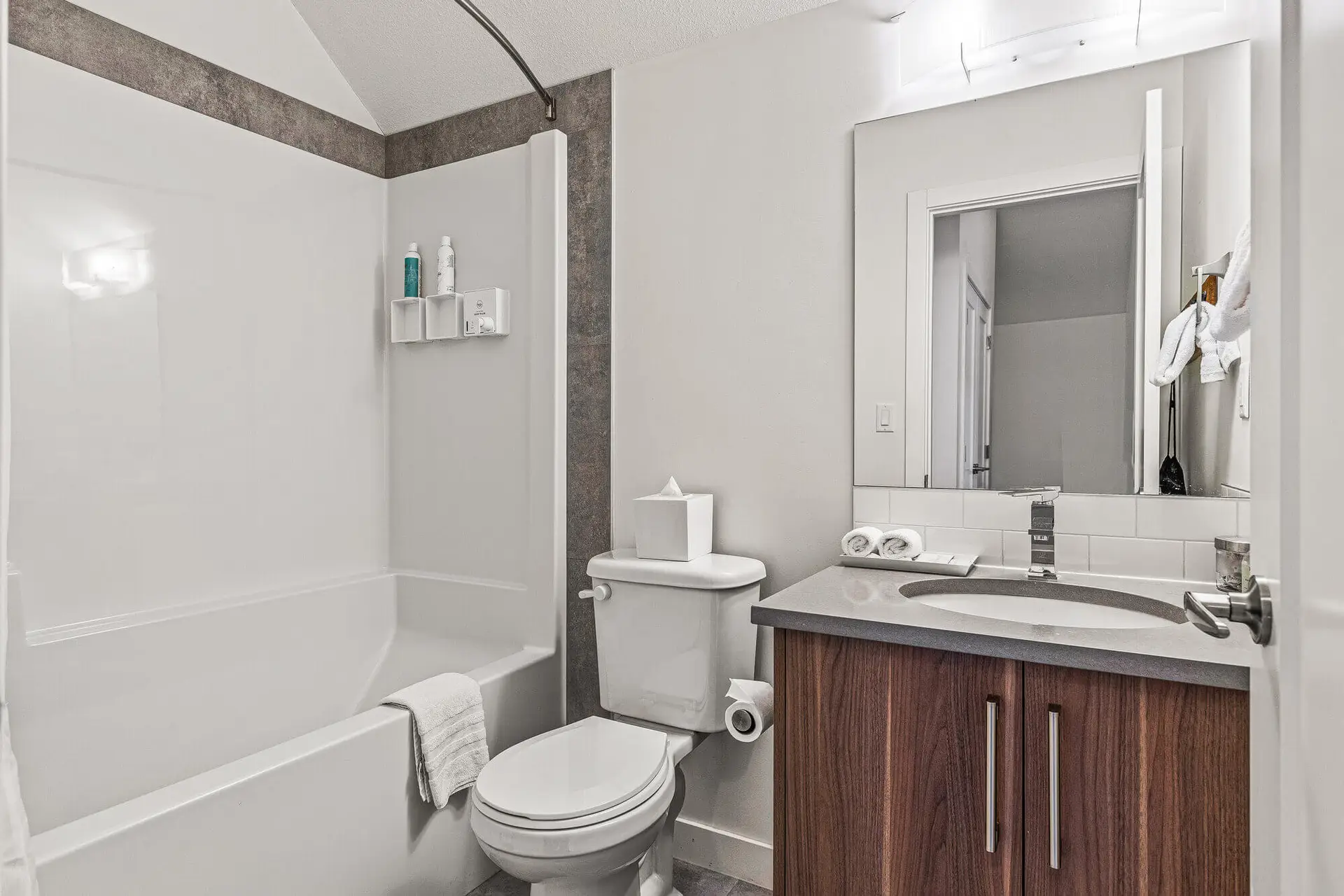 Modern bathroom with white tub, toilet, and vanity in Basecamp Resorts Canmore suite.