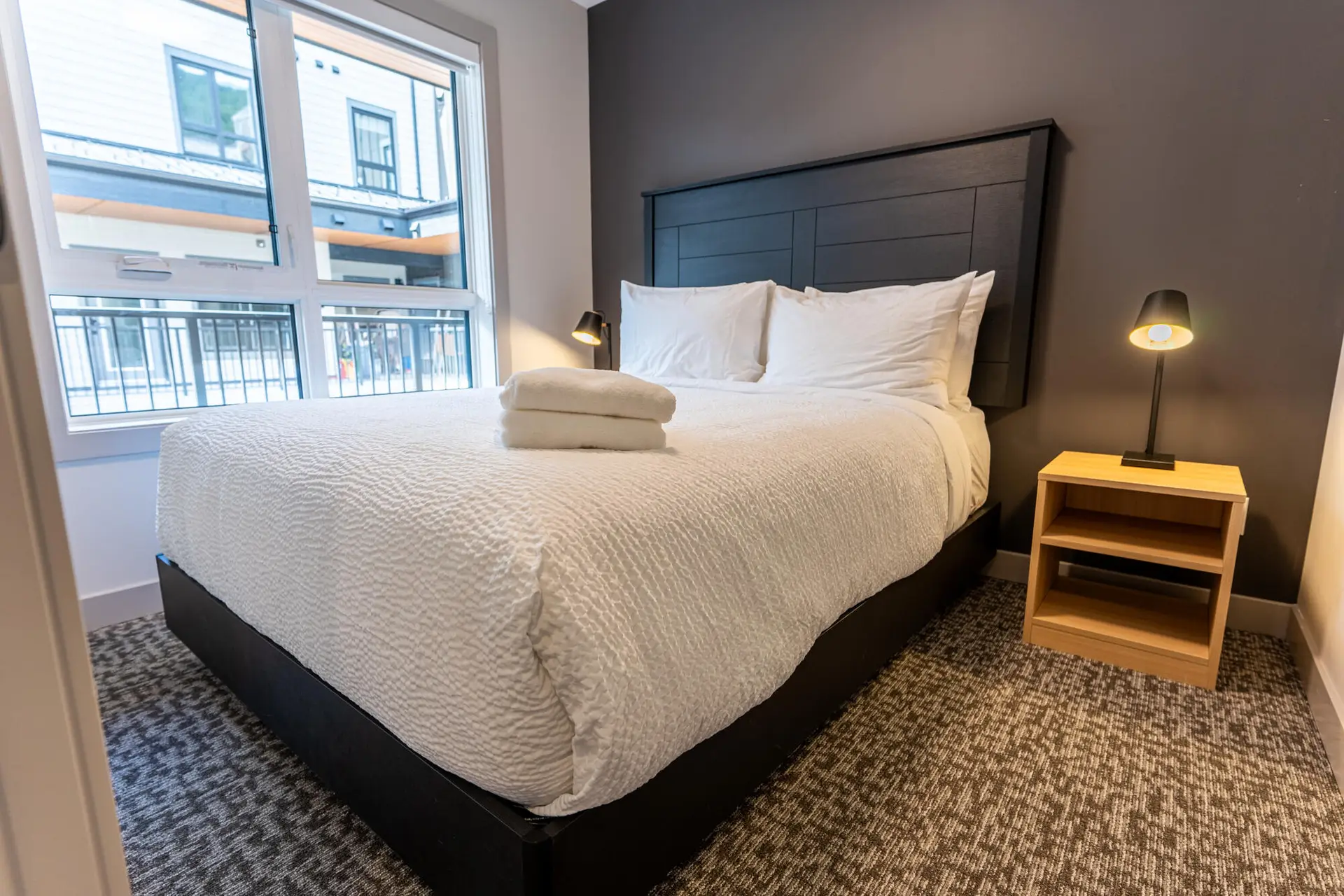 King-size bed with white linens in a hotel room at Basecamp Suites Revelstoke.