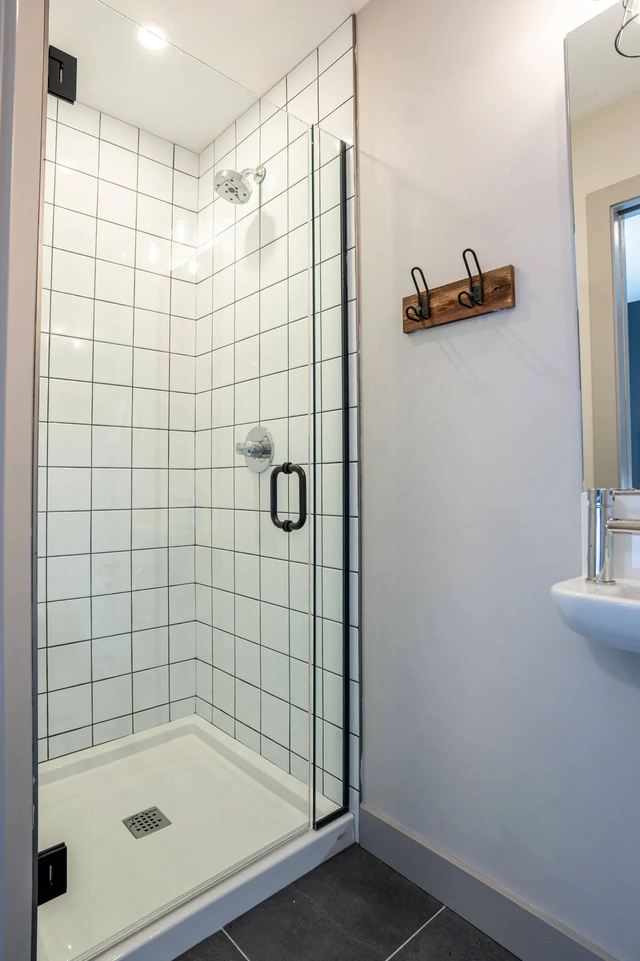 Modern white tiled shower stall with glass door in Basecamp Suites Revelstoke.