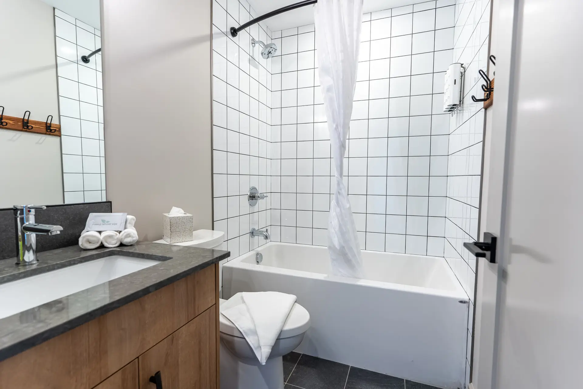Modern bathroom with white tiled shower, bathtub, and vanity in a Revelstoke suite.