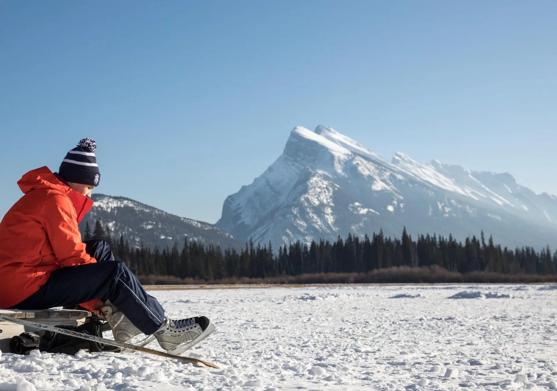 Man in orange jacket tying skates on frozen lake, Banff winter activities for non-skiers