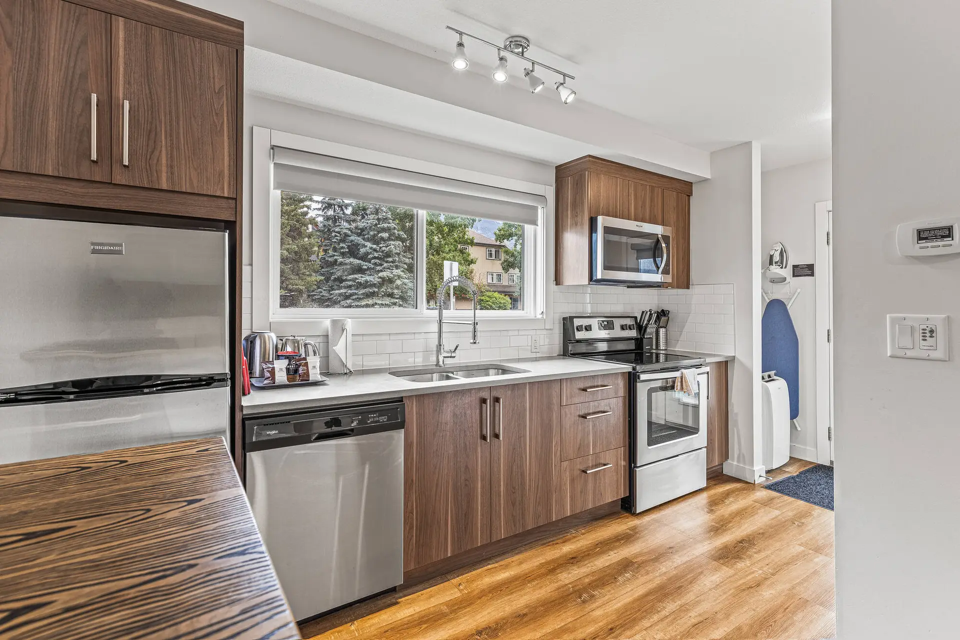 Modern kitchen with stainless steel appliances, wood cabinets, and a large window overlooking trees.