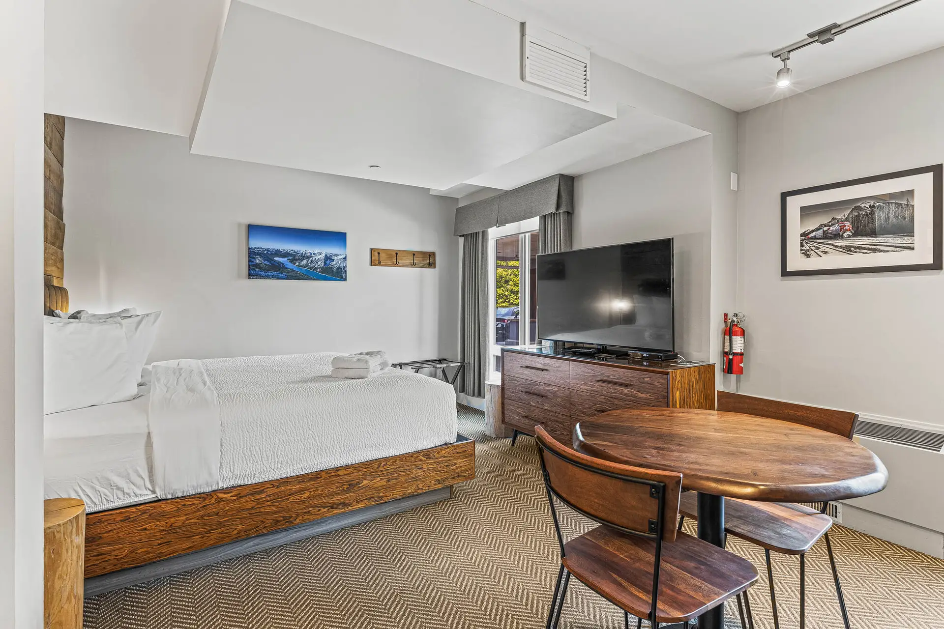 Basecamp Lodge Canmore micro suite: bed, TV, dining table, and mountain art.