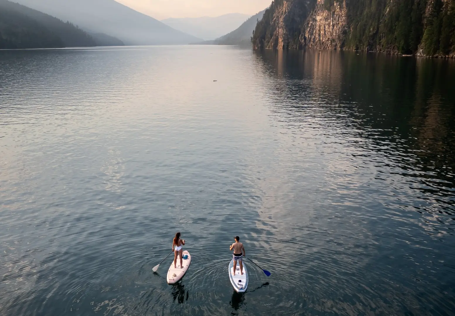 Couple paddleboarding on a serene lake near Revelstoke mountains