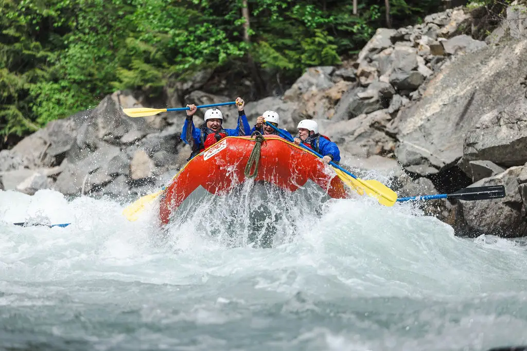 Apex Rafting: Four people in a raft navigate whitewater rapids with paddles.