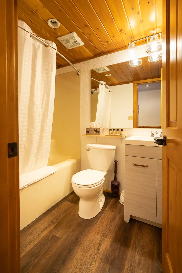 Bathroom in Basecamp Baker Creek cabin with wood ceiling, tub, toilet, and sink.