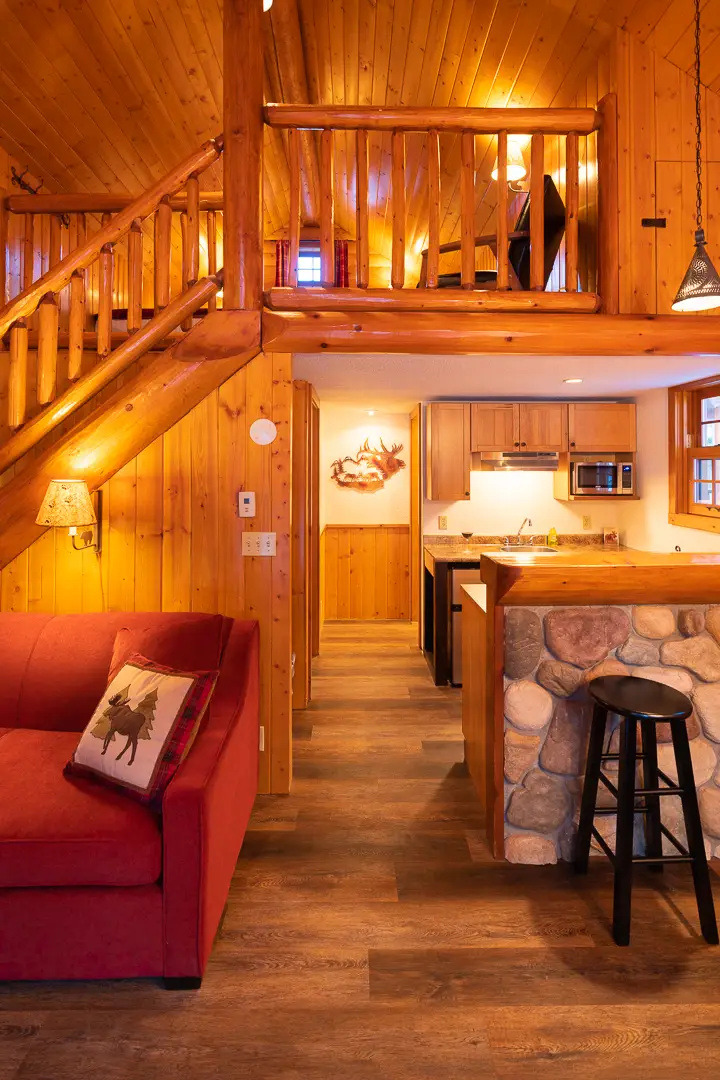 Interior of a cozy wood cabin with a loft, showing a red sofa and kitchen area
