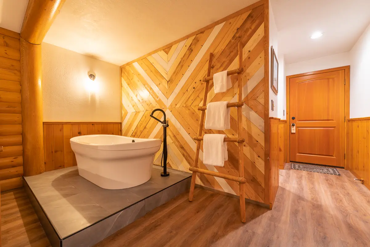 Basecamp Baker Creek Jacuzzi Suite: White soaking tub with wooden accent wall and ladder towel rack.