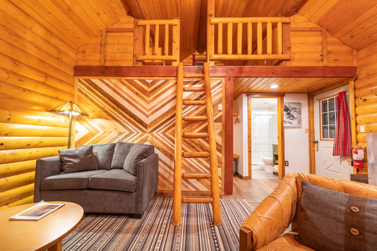 Interior of a cozy one bedroom + loft cabin with wood paneling, sofa, and ladder.