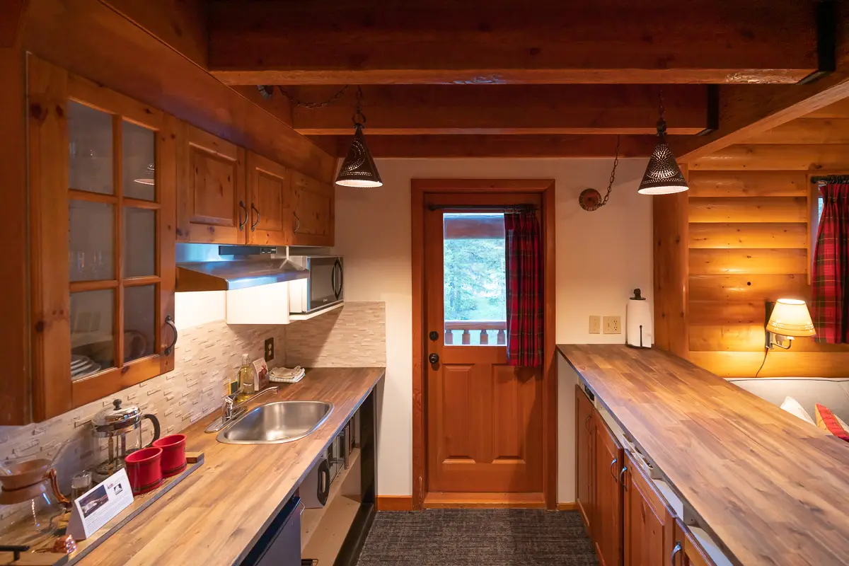 Wood-paneled kitchen in Basecamp Baker Creek Jacuzzi Suite with red plaid curtains.