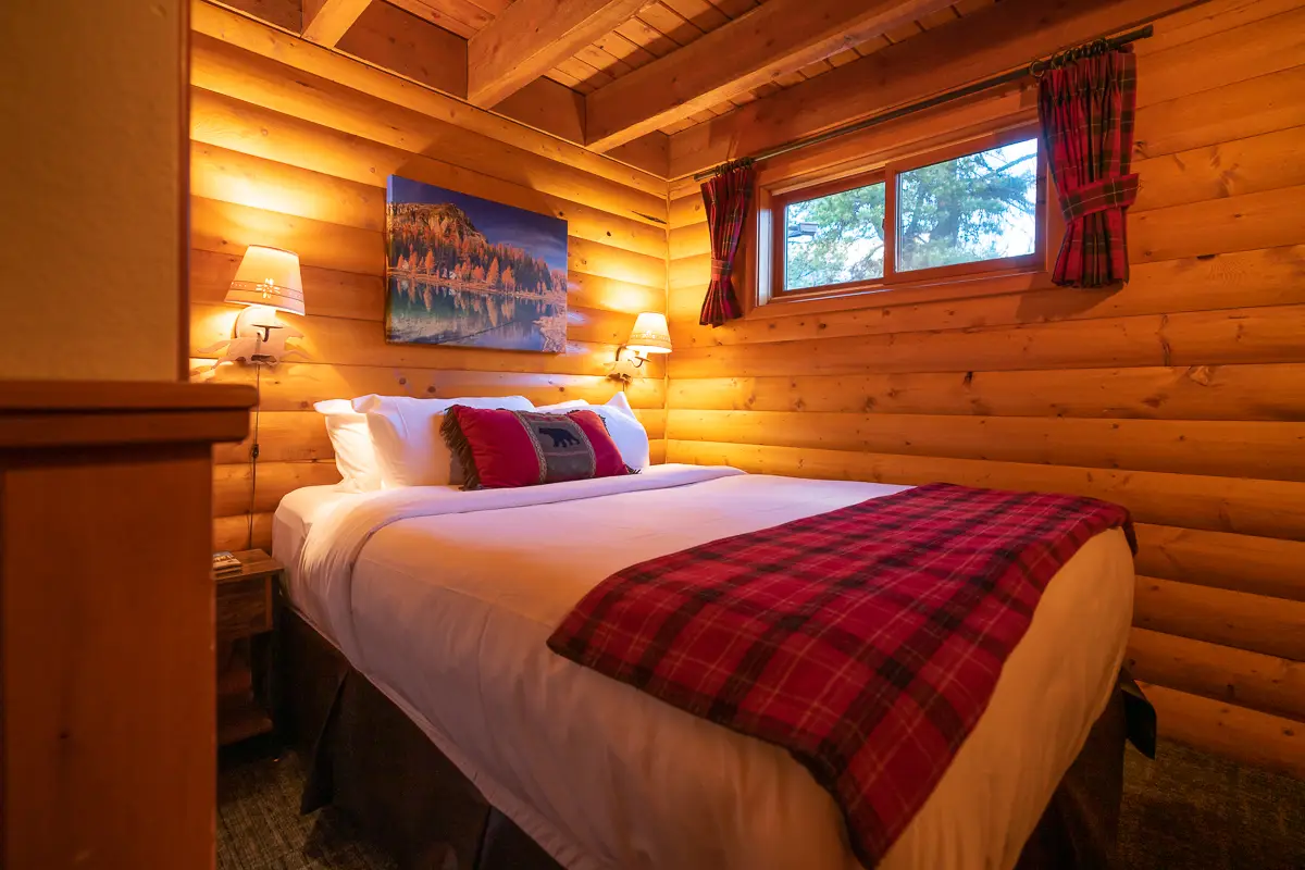 Cozy log cabin bedroom with a queen bed, plaid blanket, and mountain art