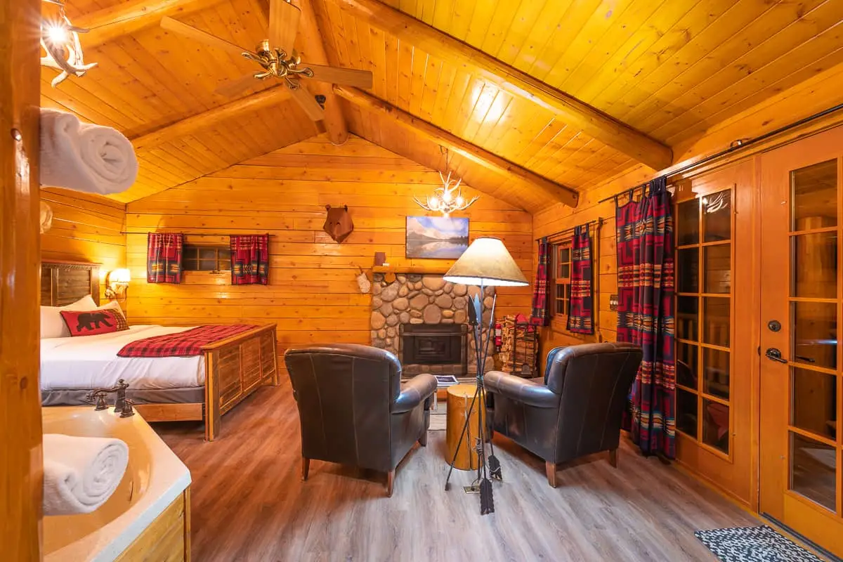 Basecamp Baker Creek Queen Cabin interior with fireplace, seating, and bed.