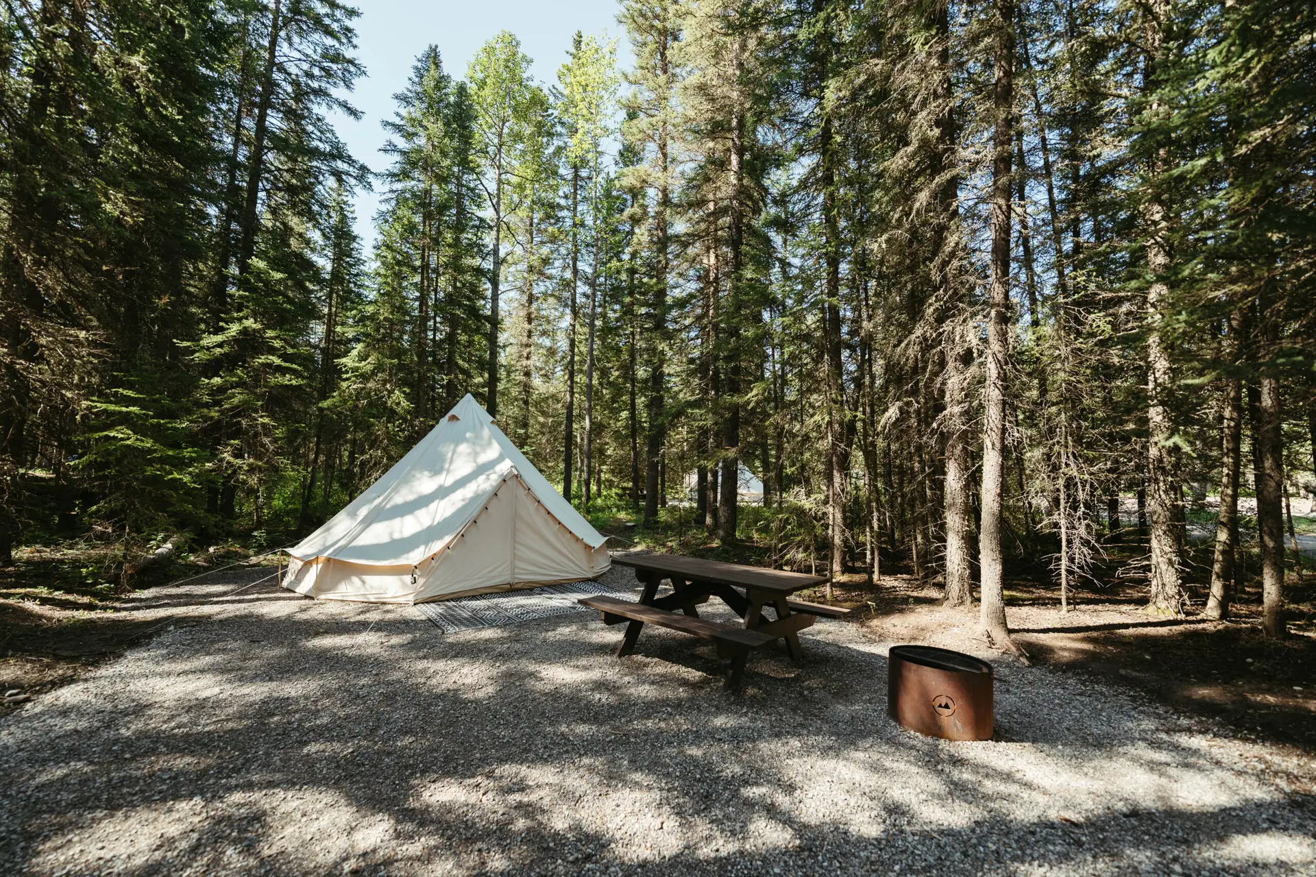 Basecamp Sundance canvas bell tent in a forest campsite with picnic table.