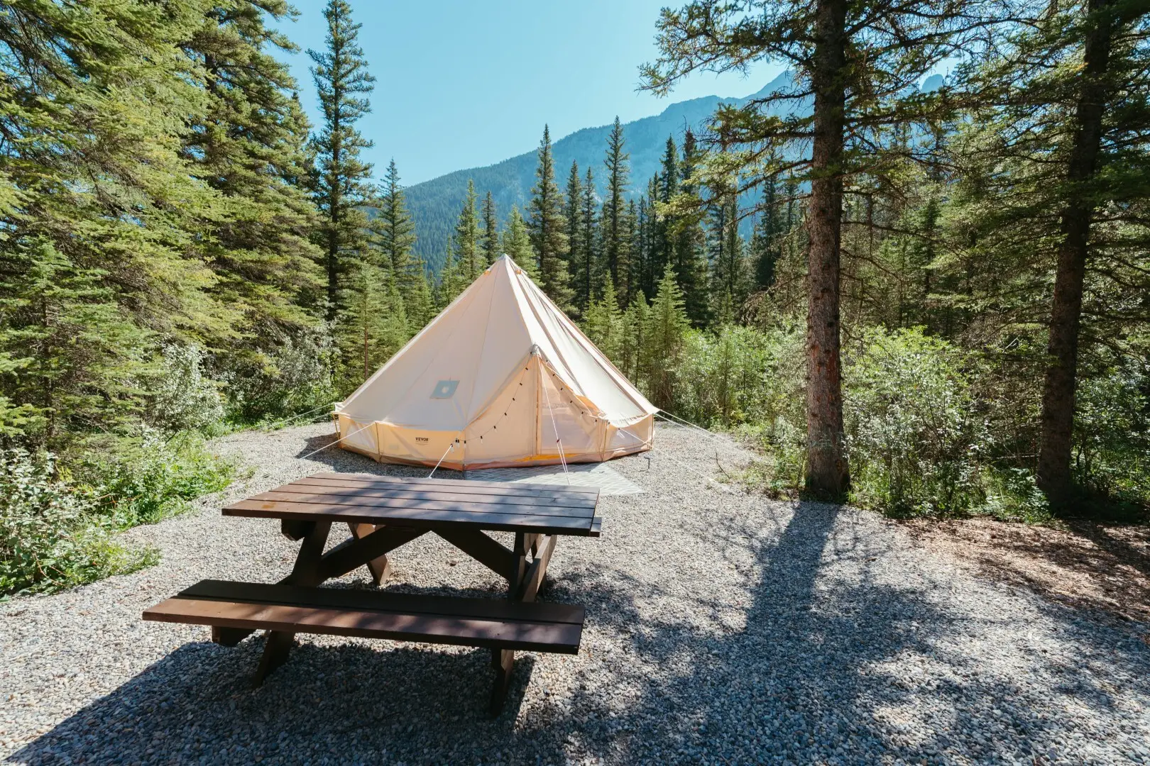Basecamp Sundance canvas bell tent pitched in a forest campsite with picnic table.