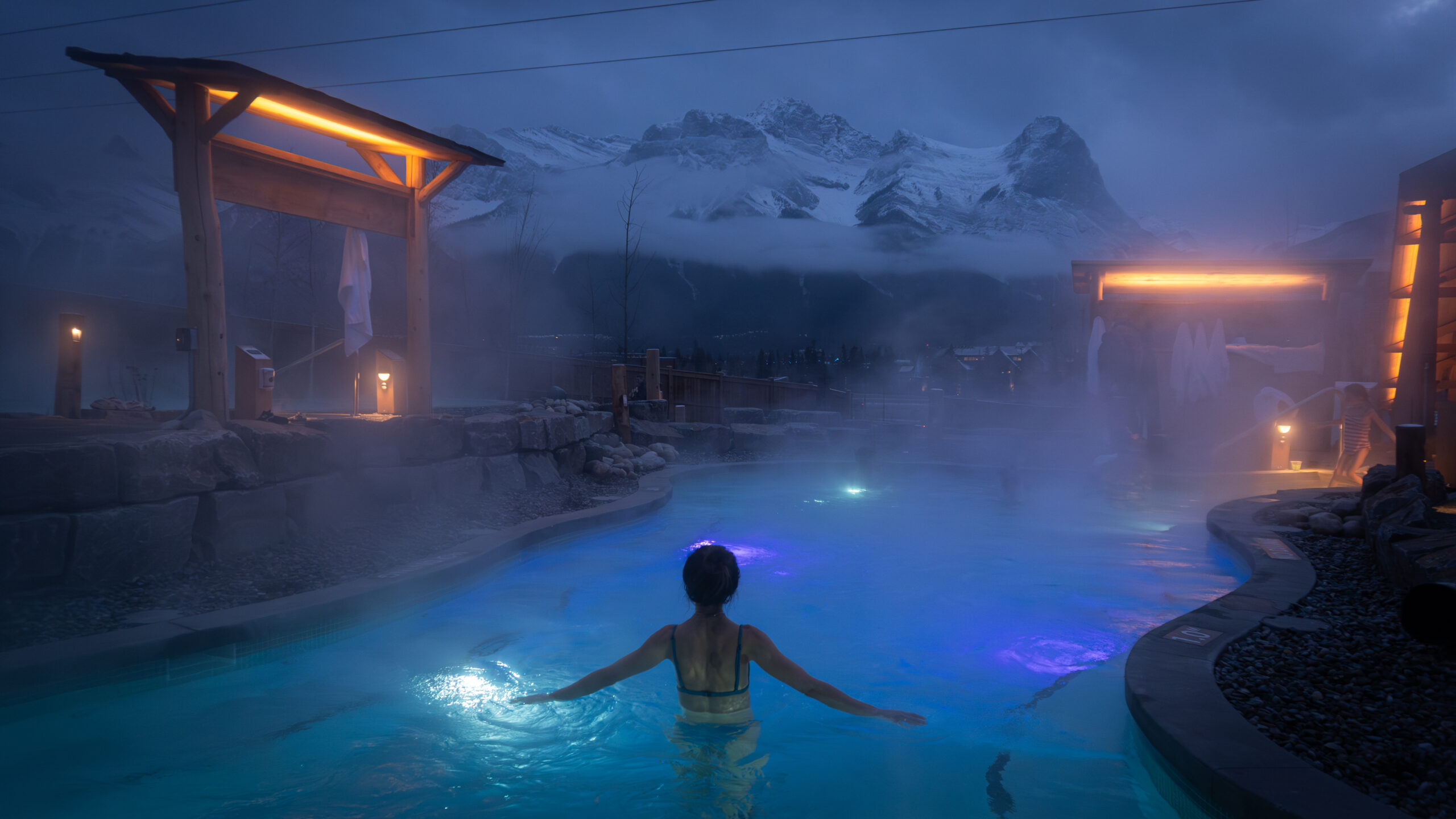 Woman relaxing in the hot pools at Everwild Canmore Nordic Spa at dusk.