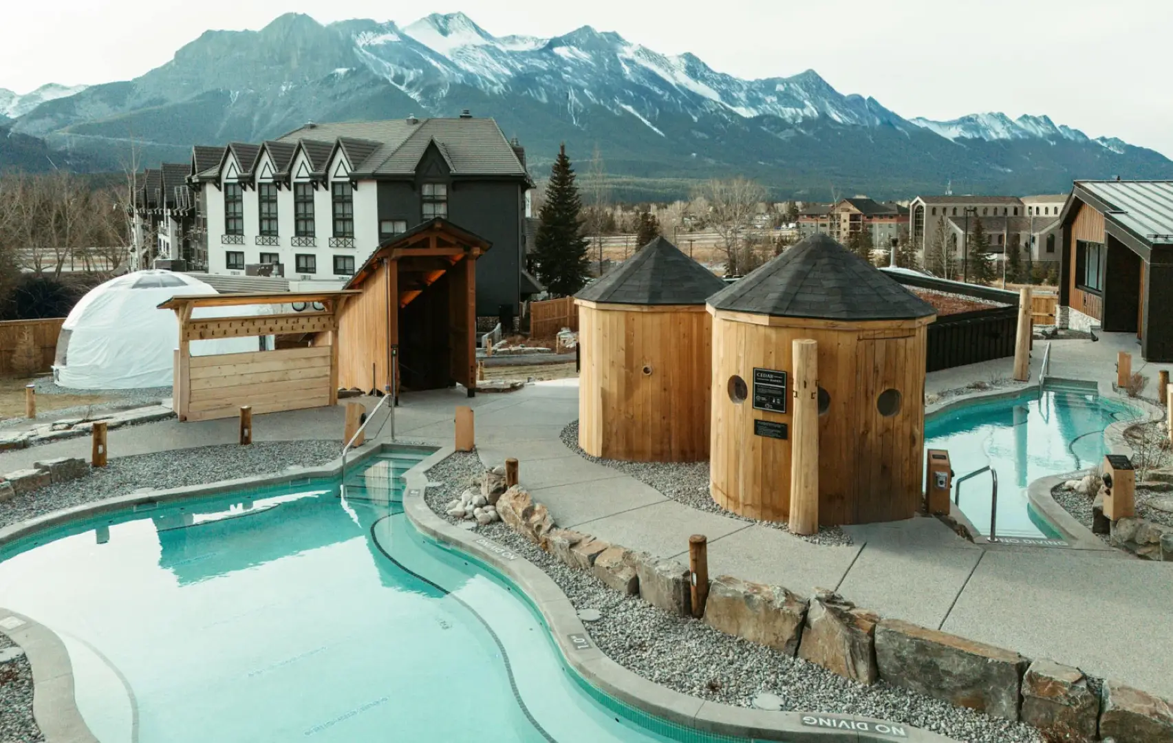 Outdoor hot springs and saunas at 1Stay Everwild with snowy mountains in the background.