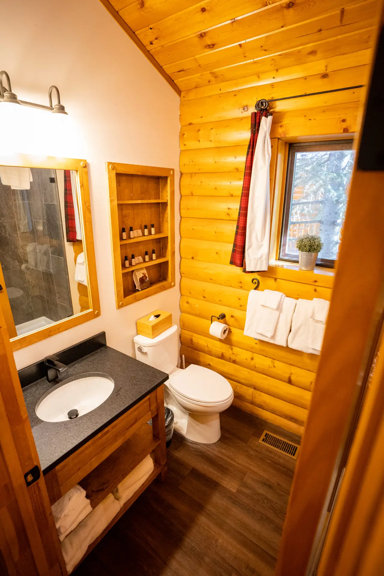 Log cabin bathroom with wood walls, sink, toilet, and shower