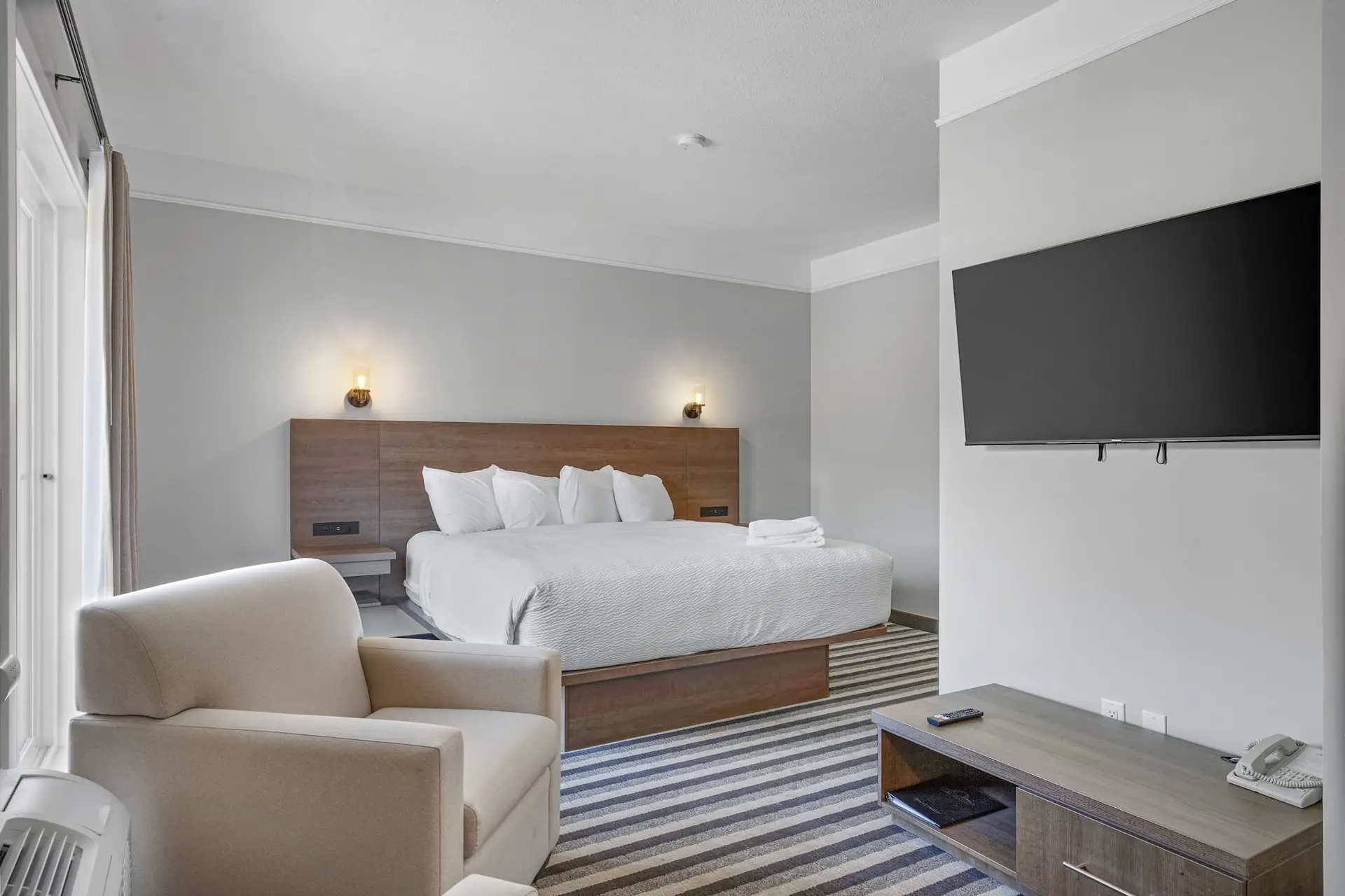 King bed with white linens, armchair, and TV in a hotel room at Basecamp Northwinds Canmore.