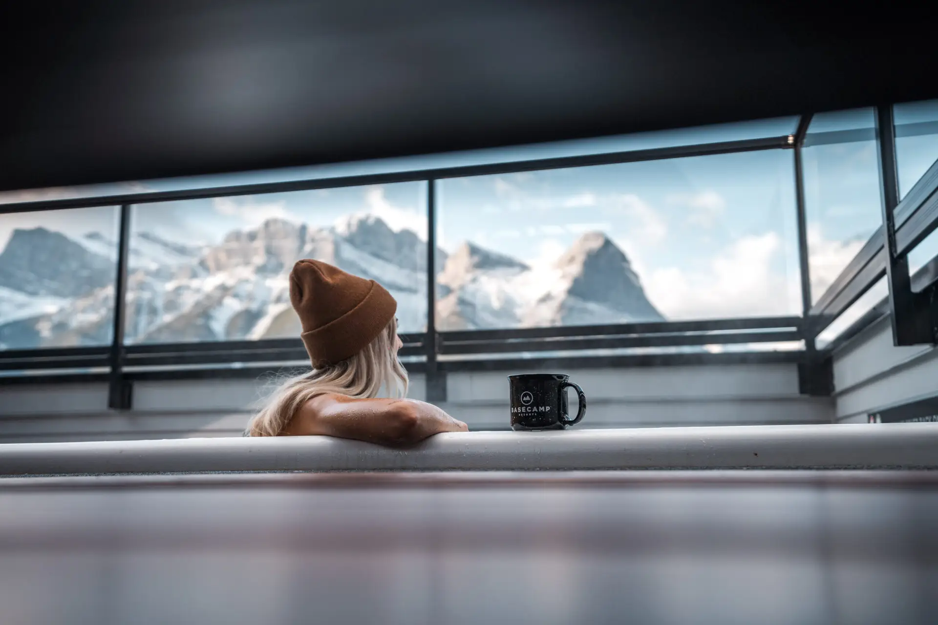 Woman in beanie relaxes in hot tub at Basecamp Resorts Canmore with mountain view