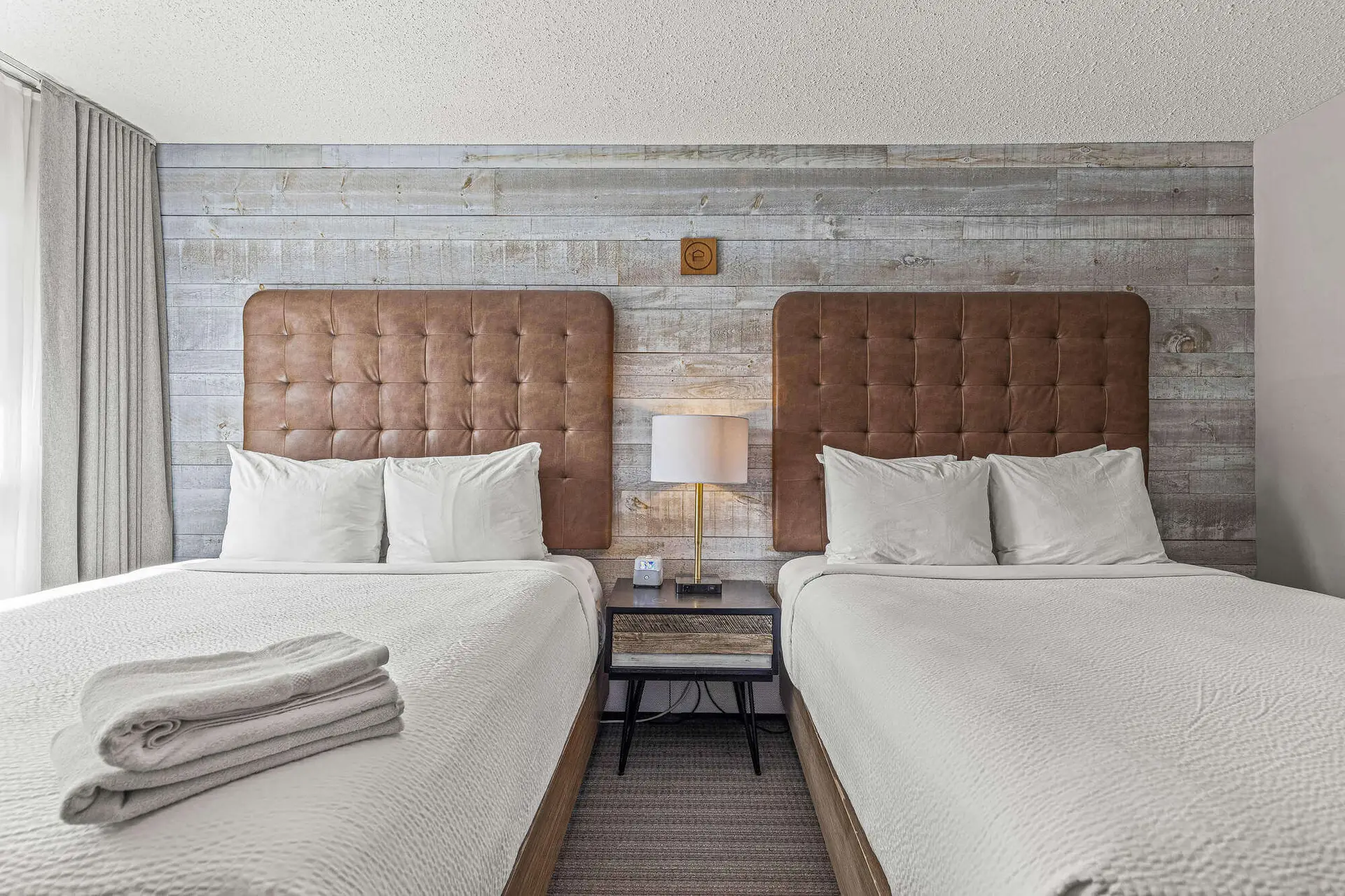 Double Queen bedroom at Basecamp Lamphouse Canmore with rustic wood wall and views.