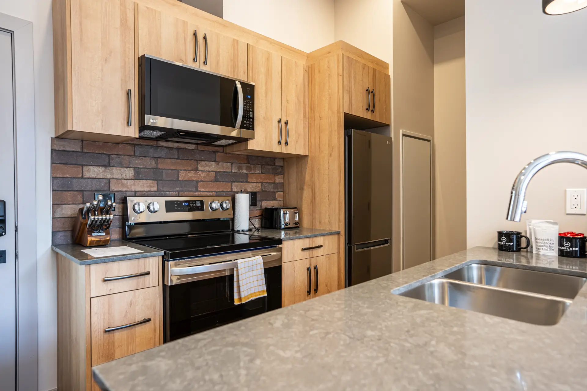 Modern kitchen in Basecamp Suites Revelstoke micro studio with wood cabinets, stainless steel appliances, and granite countertops.