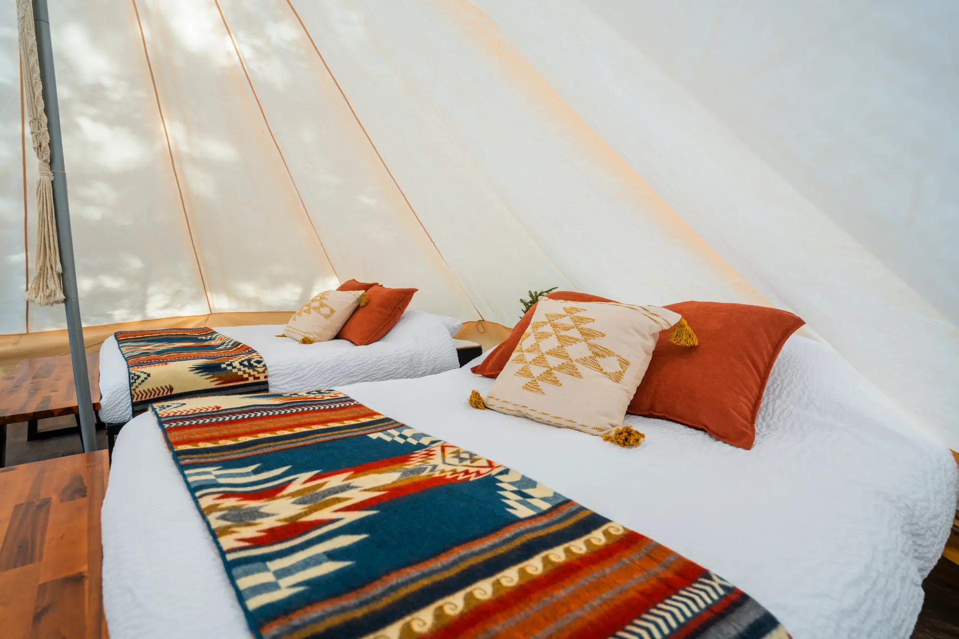 Interior of a glamping canvas tent with two beds, featuring colorful blankets and pillows.