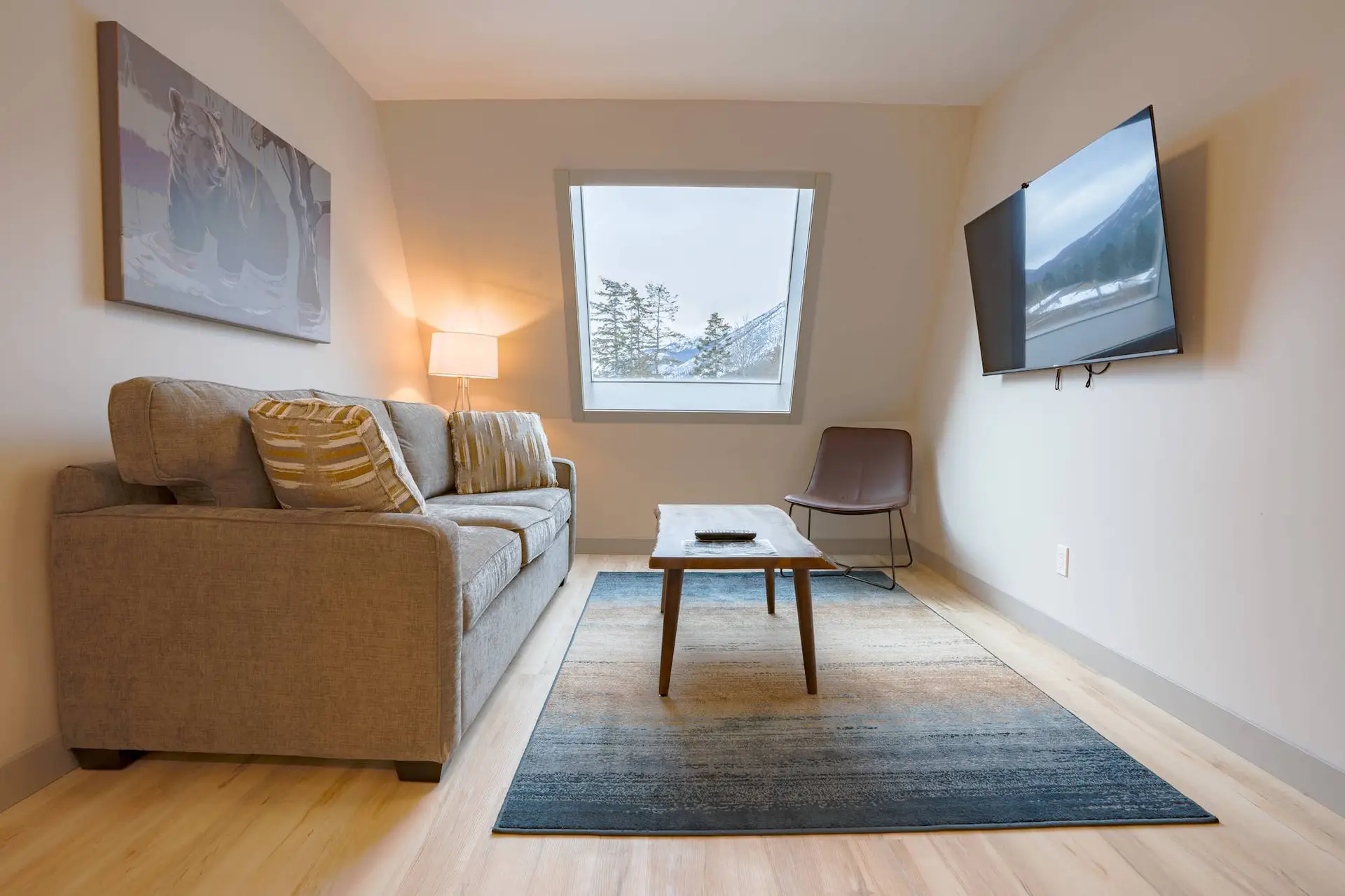 Basecamp Suites Banff Superior Two King Suite living area with sofa, coffee table, rug, chair, and mountain view window.