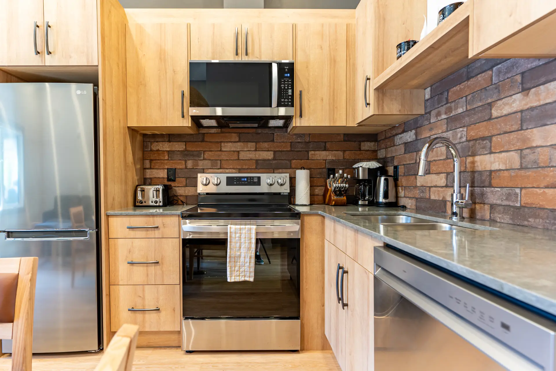 Modern kitchen in Basecamp Suites Revelstoke Superior One Bedroom Suite with stainless steel appliances and brick backsplash.