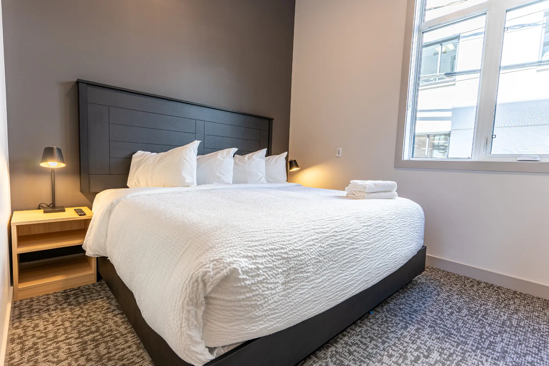 Revelstoke Basecamp Suites: King bed with white linens, bedside lamps, and window view