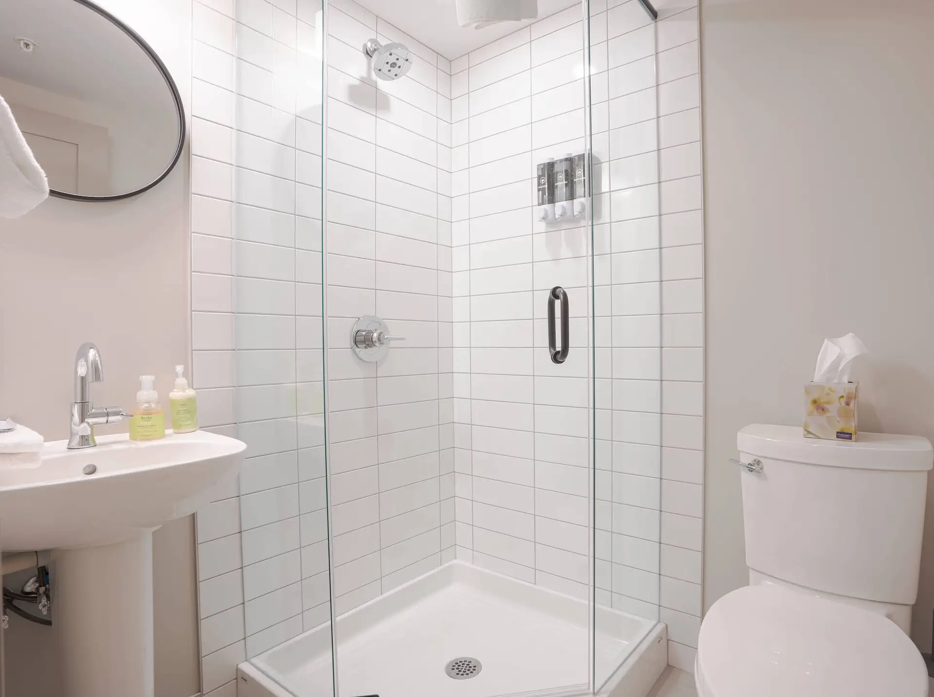 Modern bathroom with white tiled shower, pedestal sink, and toilet at Basecamp Suites Banff.