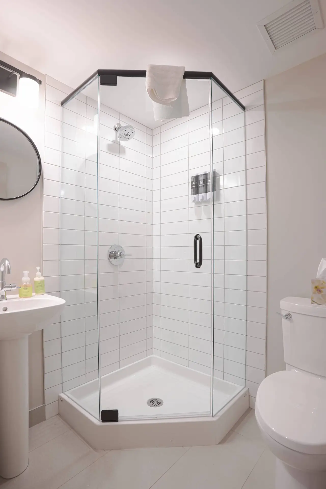 Modern white tiled corner shower with glass doors in a hotel bathroom.