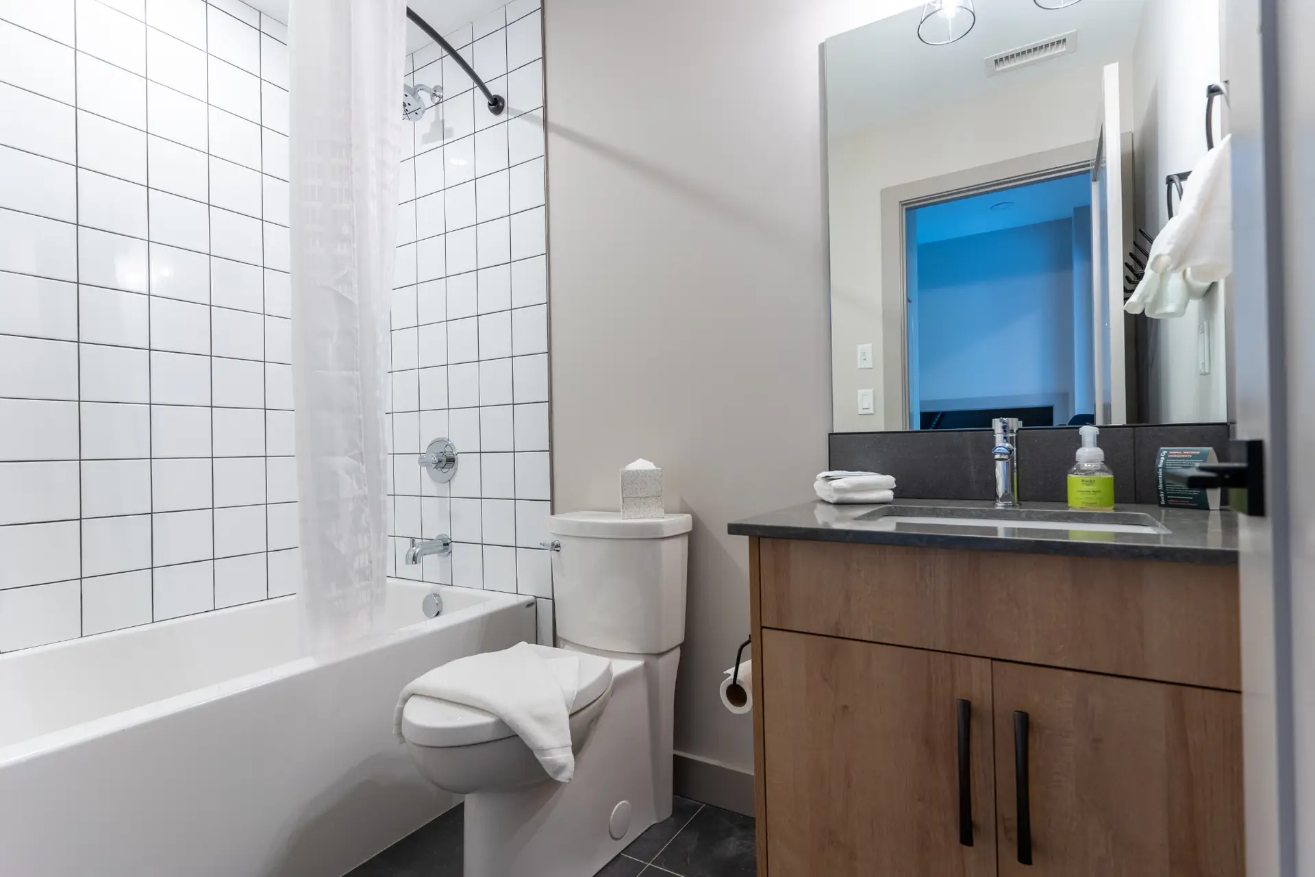 Modern bathroom with white tiled shower, toilet, and wooden vanity in Basecamp Suites Revelstoke.