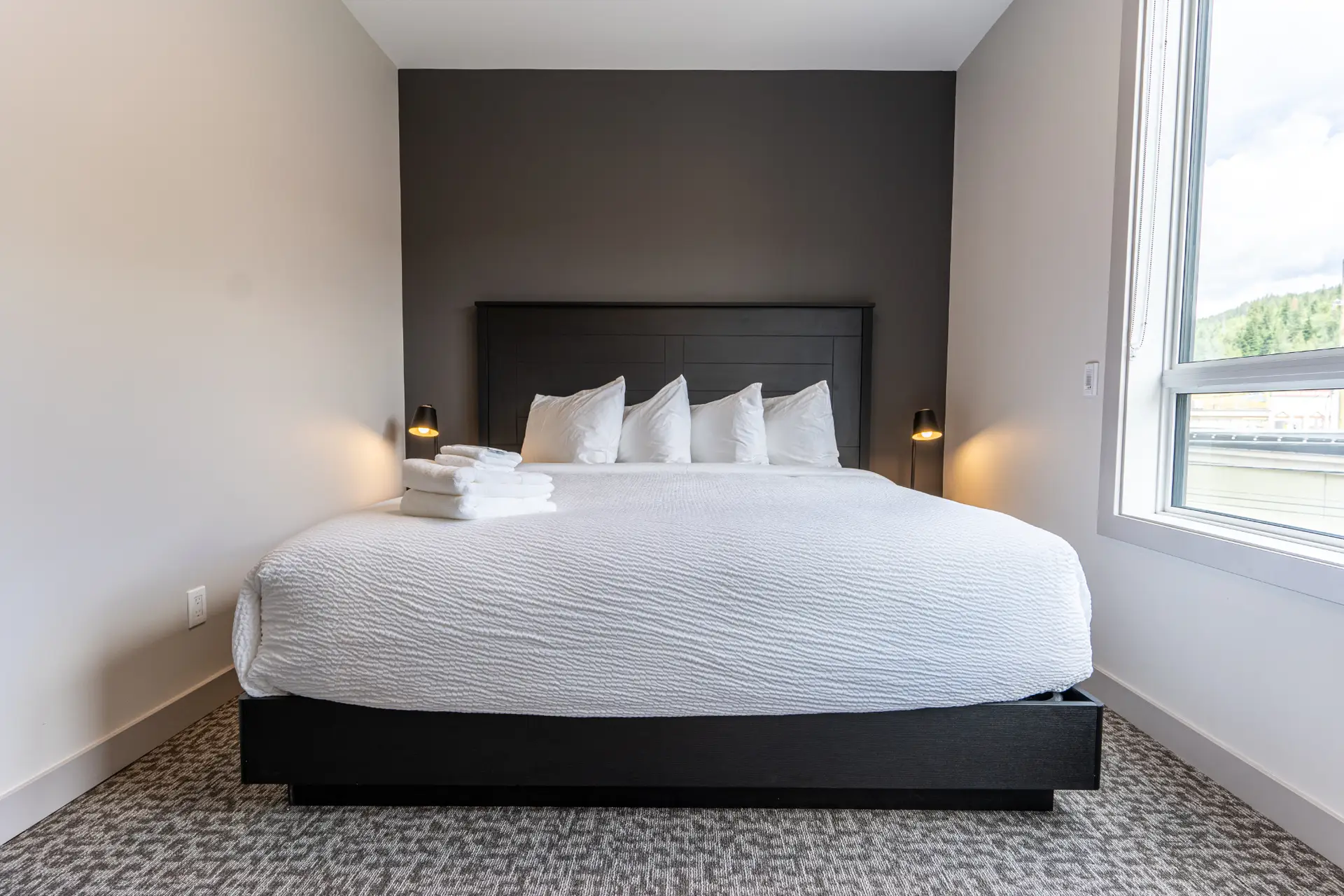 King-size bed with white linens and pillows in a modern hotel room at Basecamp Suites Revelstoke.