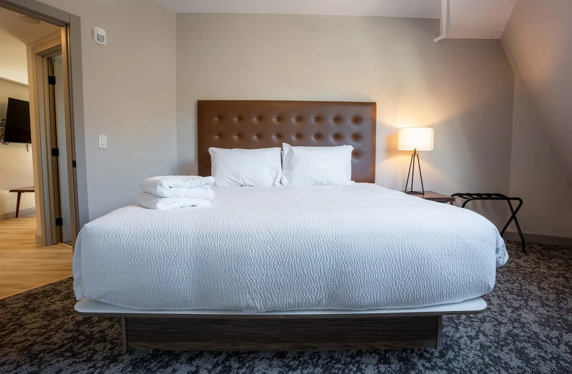 King-size bed with white linens and brown tufted headboard in a hotel suite.