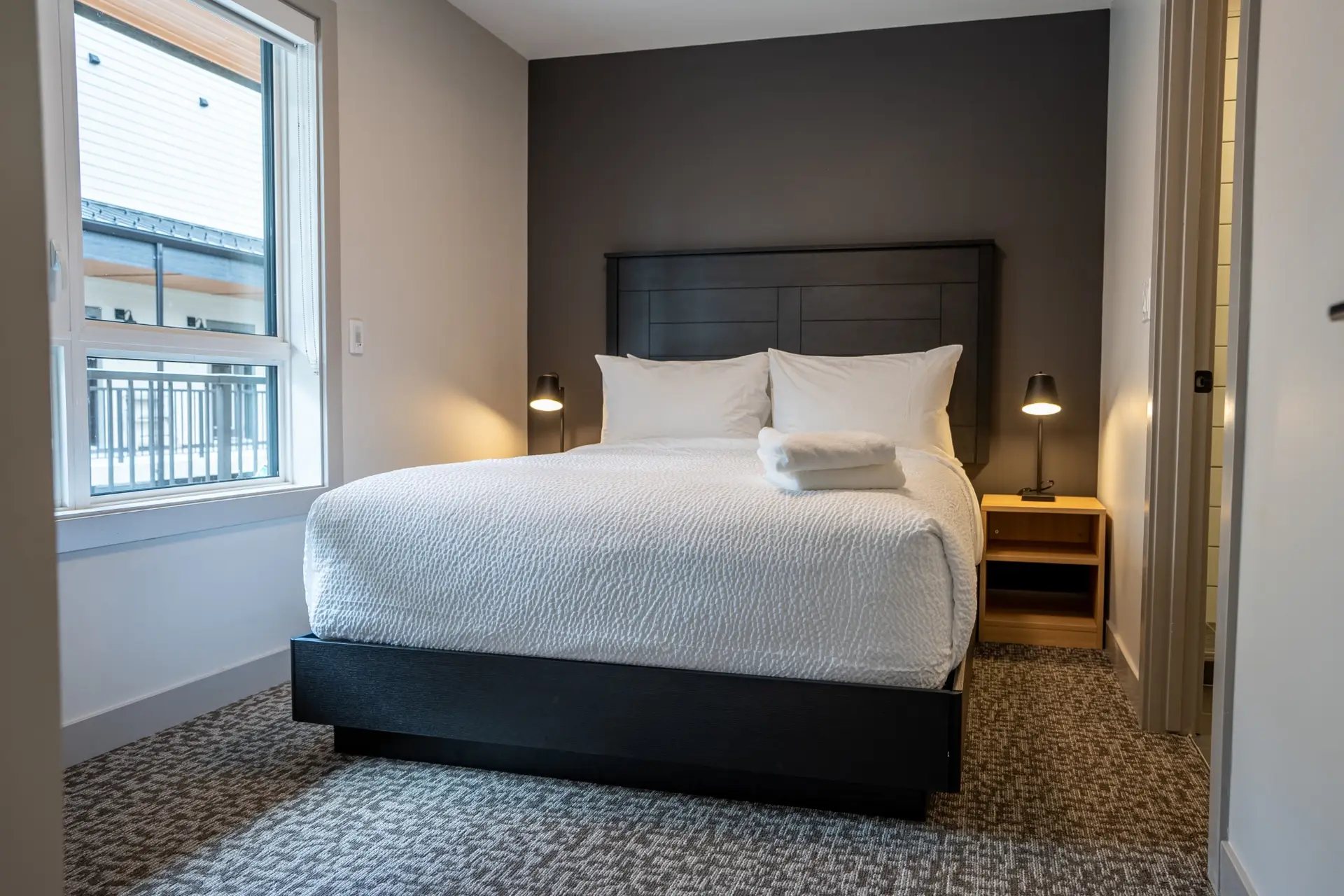 King-size bed with white linens in a modern hotel room at Basecamp Suites Revelstoke.