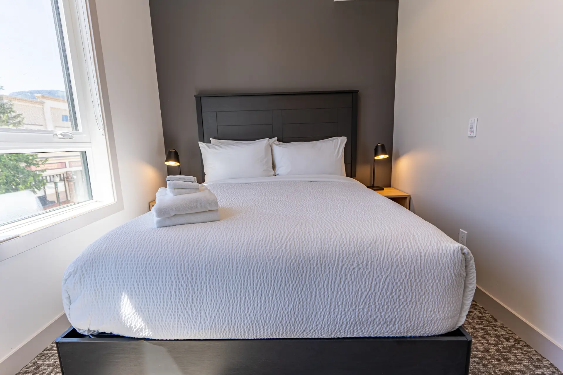 Queen bed with white linens and stacked towels in a modern hotel suite