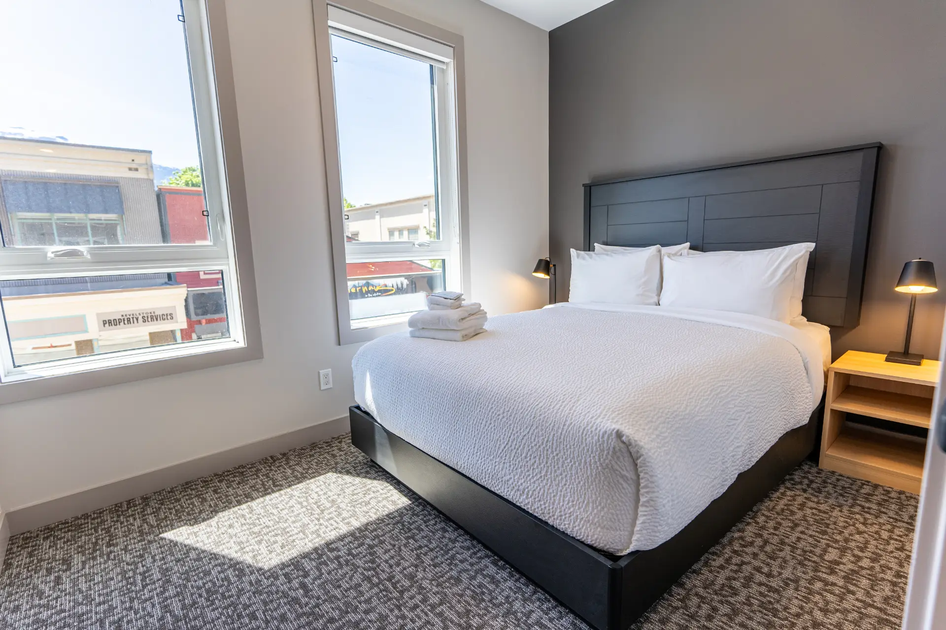 Queen bed with white linens in a modern hotel room at Basecamp Suites Revelstoke.