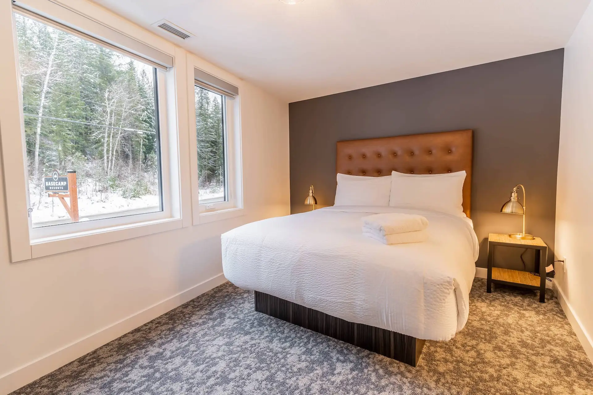 Basecamp Resorts Revelstoke suite bedroom with queen bed, windows overlooking forest