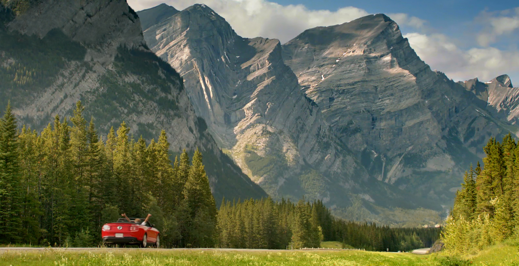 Red convertible road trip in Canadian Rockies with mountains and pine trees