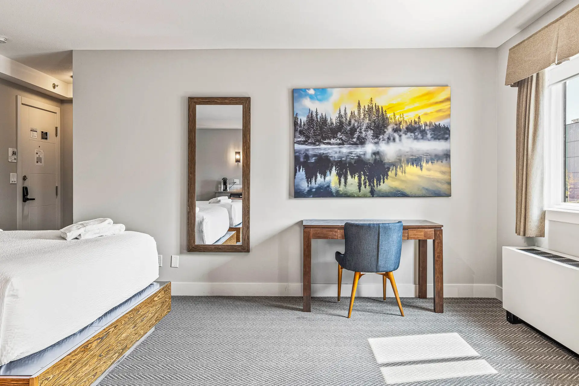 Deluxe double king room at Basecamp Lodge Canmore with a bed, desk, and mountain landscape art.