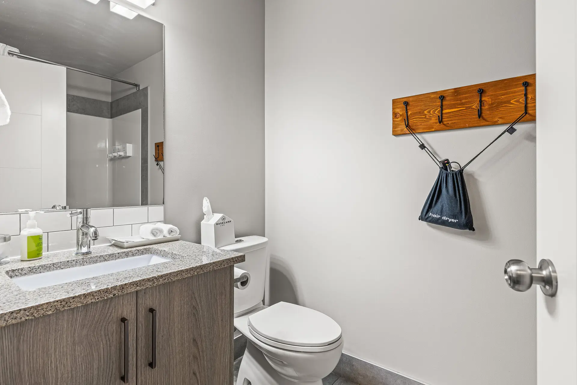 Modern bathroom at Basecamp Lodge Canmore with vanity, toilet, and wall-mounted hairdryer.