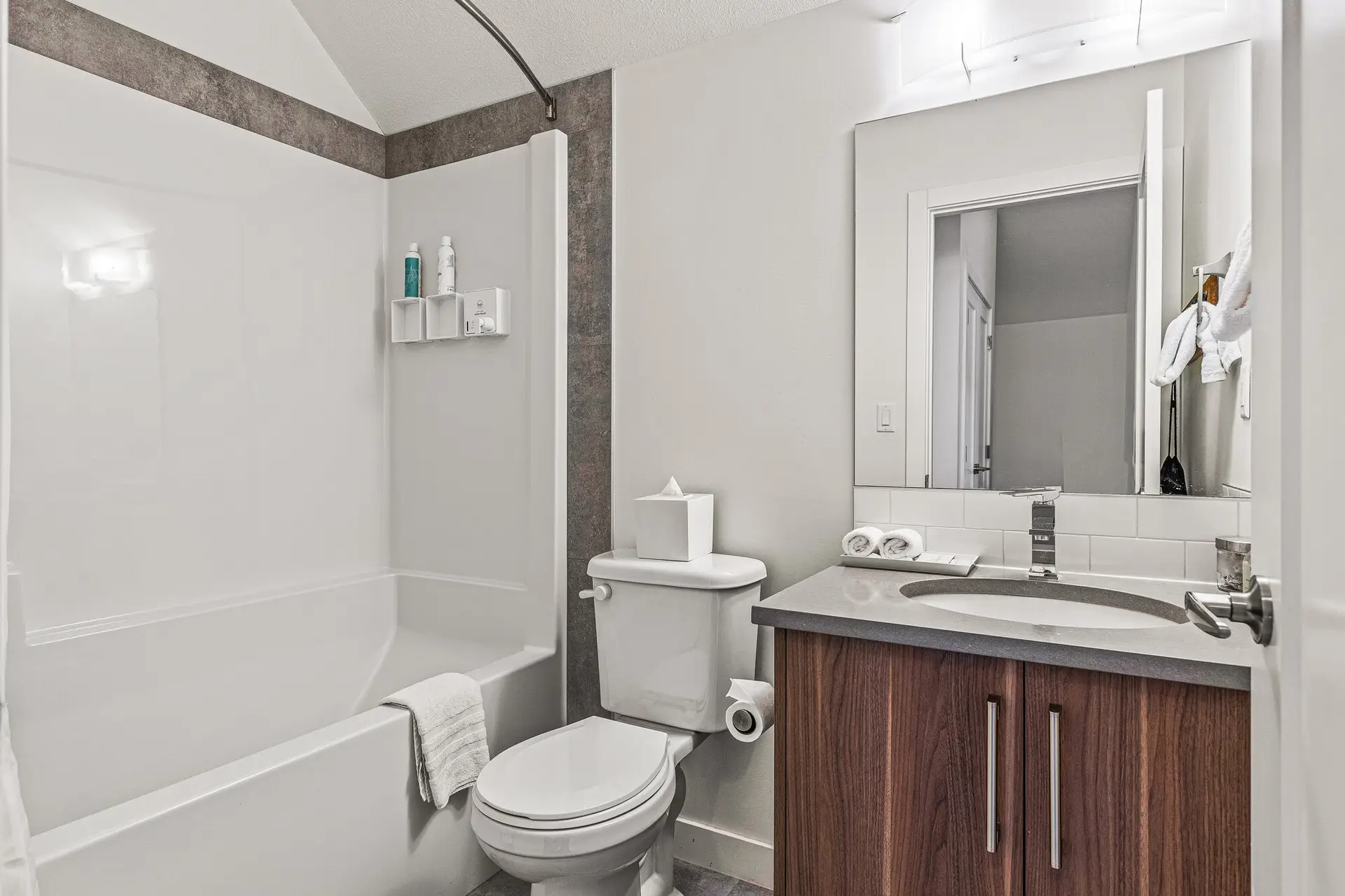 Modern hotel bathroom with white tub, toilet, and vanity at Basecamp Resorts Canmore.