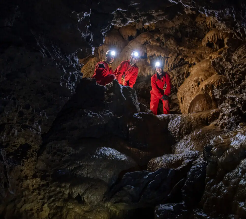 Three cavers in red suits with headlamps explore a cave in Canmore