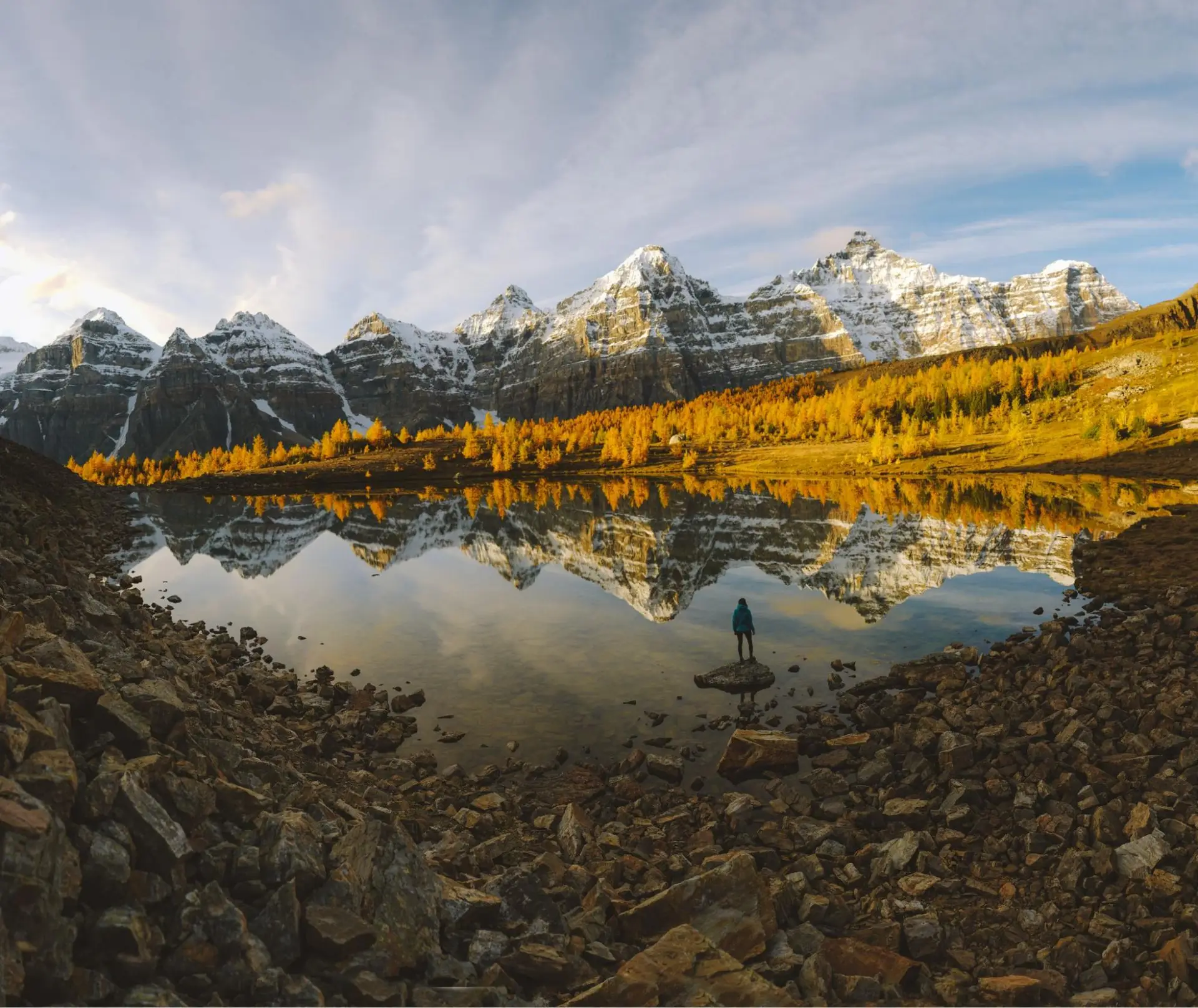 Golden larches frame a serene lake reflecting snow-capped Canadian Rockies mountains.