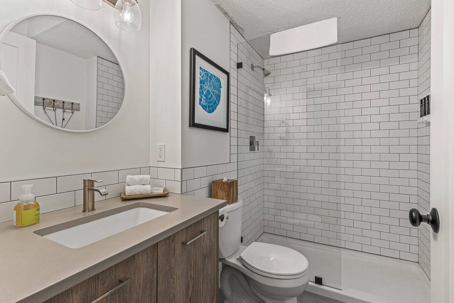 Modern bathroom with white tiles, wooden cabinet, and a glass shower